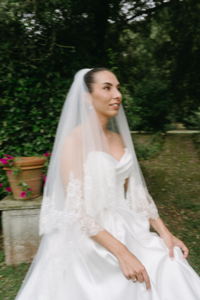 Bride in white dress and veil walking through a garden before her Tuscany elopement ceremony