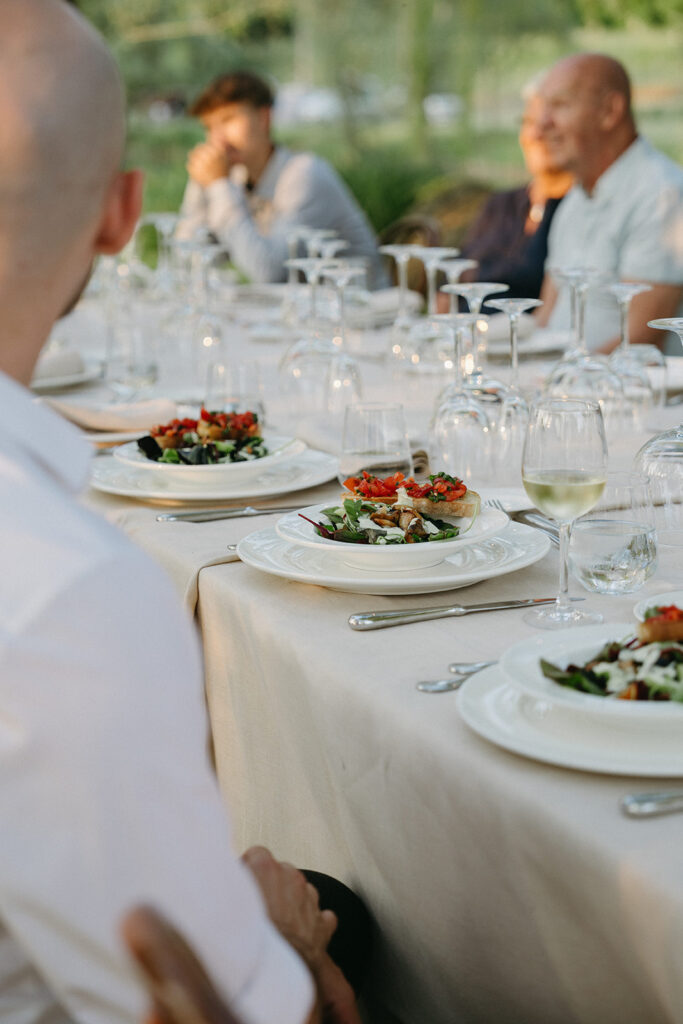 Traditional Tuscan wedding dinner with bruschetta, salad, and white wine under the evening sun