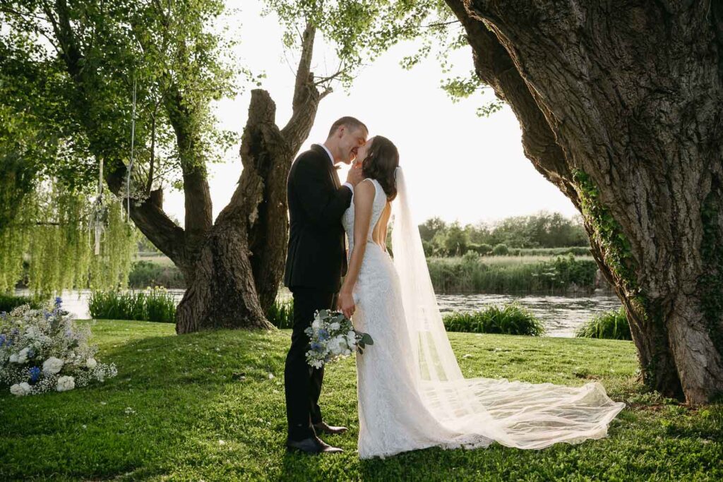 Newlyweds sharing a kiss beside the river in golden light at La Finestra Sul Fiume