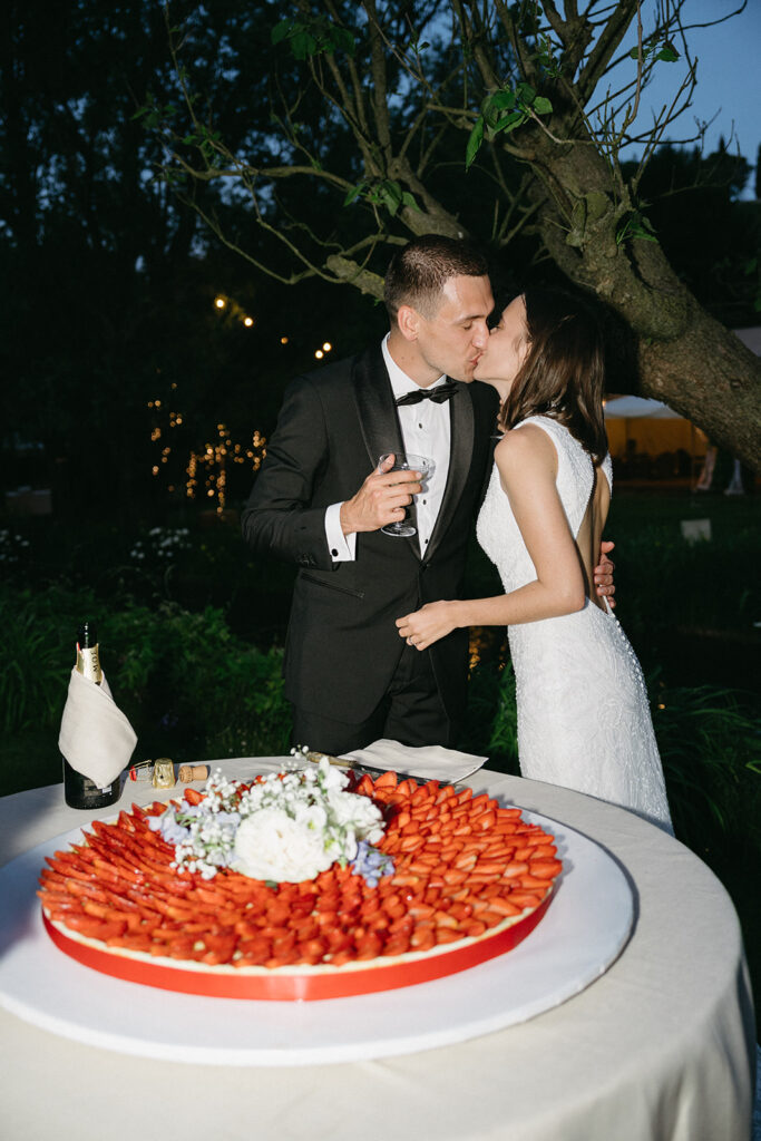 Newlyweds share a kiss beside strawberry wedding cake